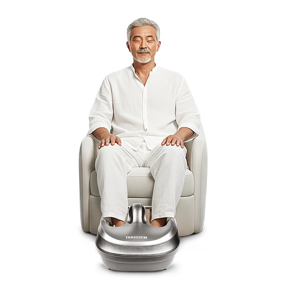 Пожилой мужчина в белом костюме сидит в кресле, положив ноги в массажер для ног Yamaguchi Mojo серого цвета
