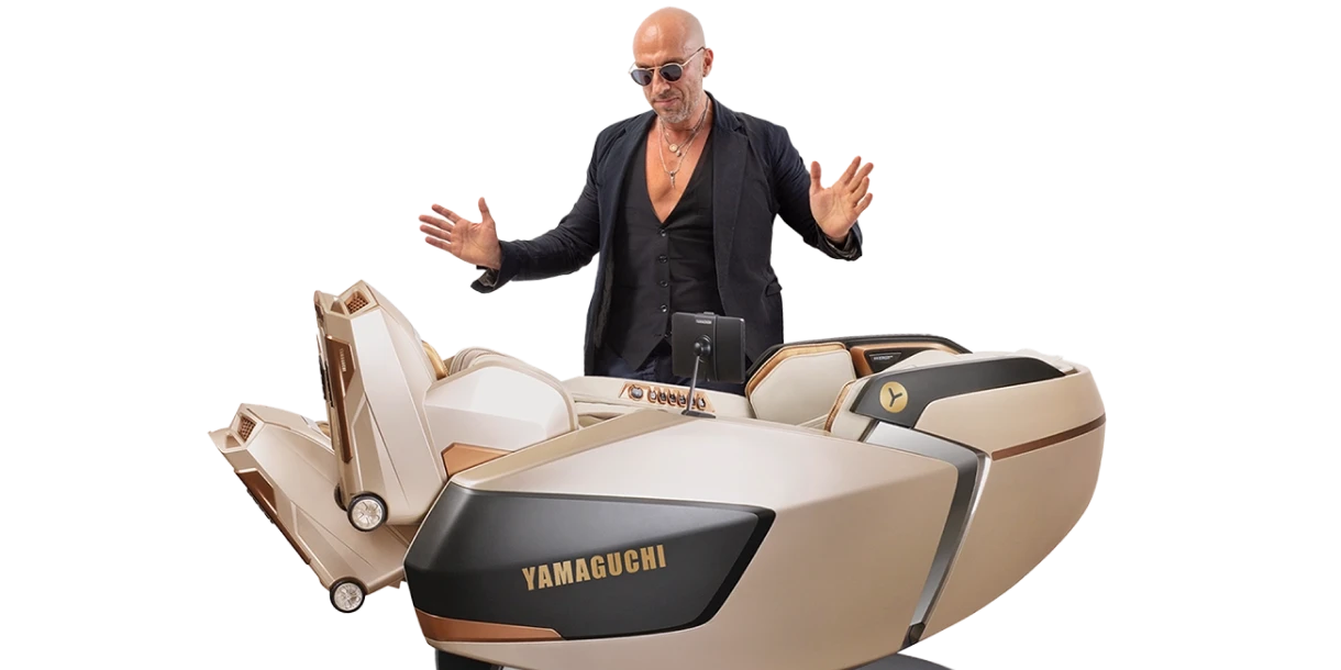 Дмитрий Нагиев в чёрном пиджаке стоит рядом с золотым массажным креслом Yamaguchi Xi Robot, демонстрируя его функции