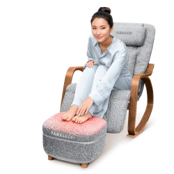 Женщина в белой пижаме сидит в массажном кресле Yamaguchi Liberty Comfort, положив ноги на Yamaguchi Capsula Grey